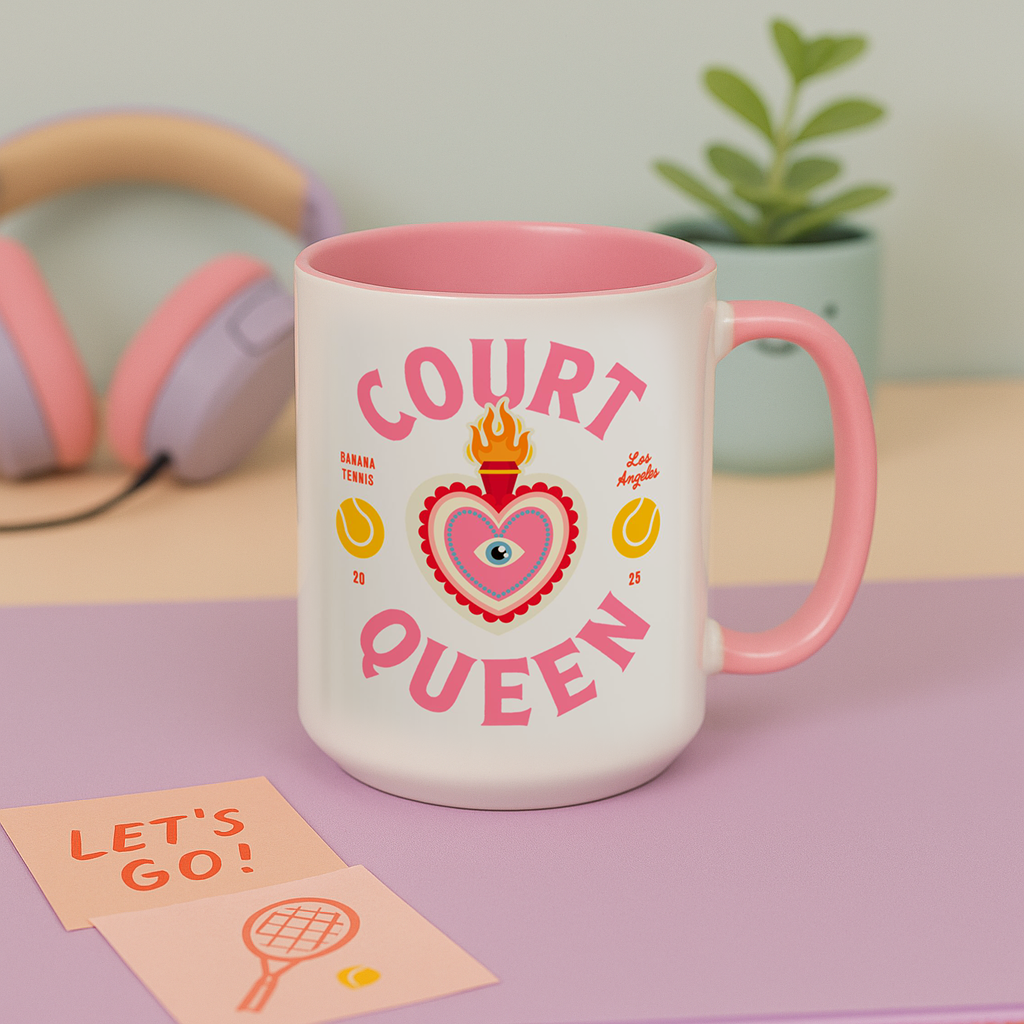 Pink and white mug with 'Court Queen' design on a table with headphones and a plant in the background