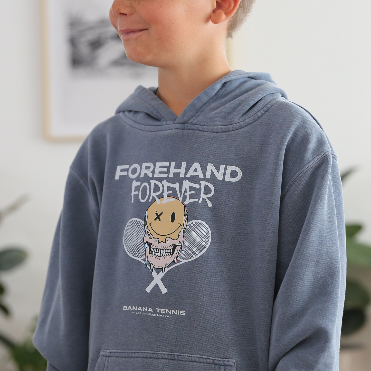 A child wearing a steel blue hoodie with 'FOREHAND FOREVER' text and a cartoon tennis character on the front.
