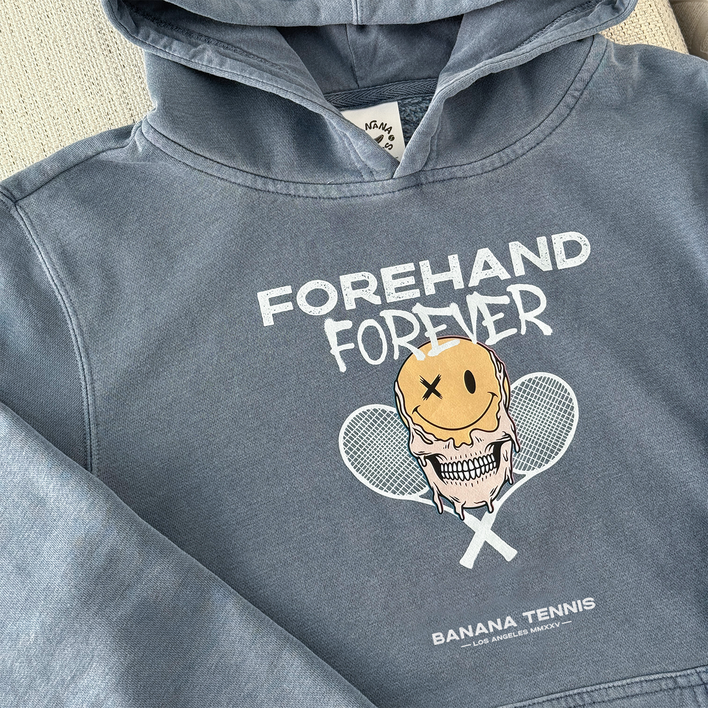 Blue hoodie with 'Forehand Forever' graphic design on a beige surface