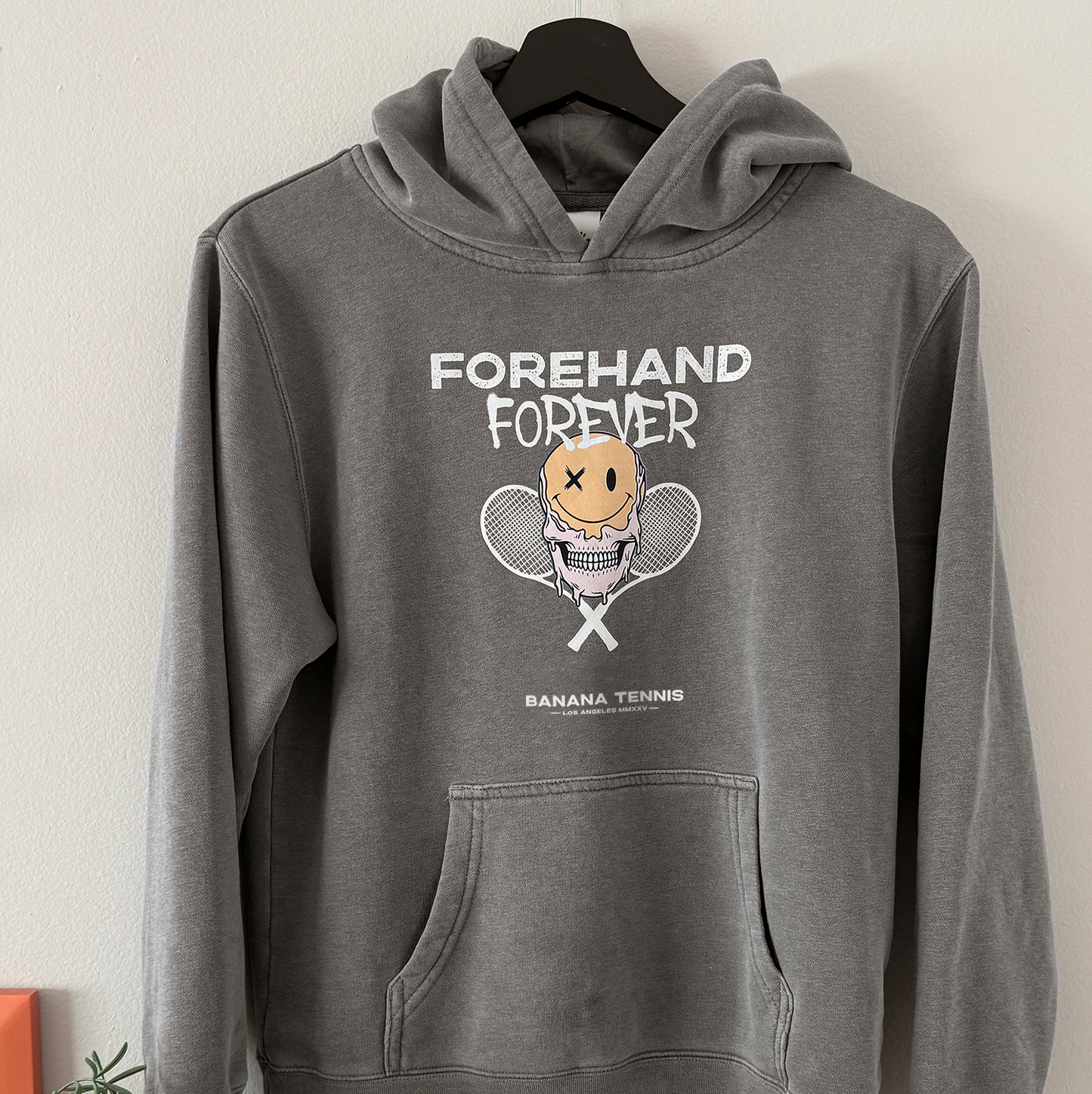 Gray hoodie with 'Forehand Forever' graphic design on a hanger against a white wall.