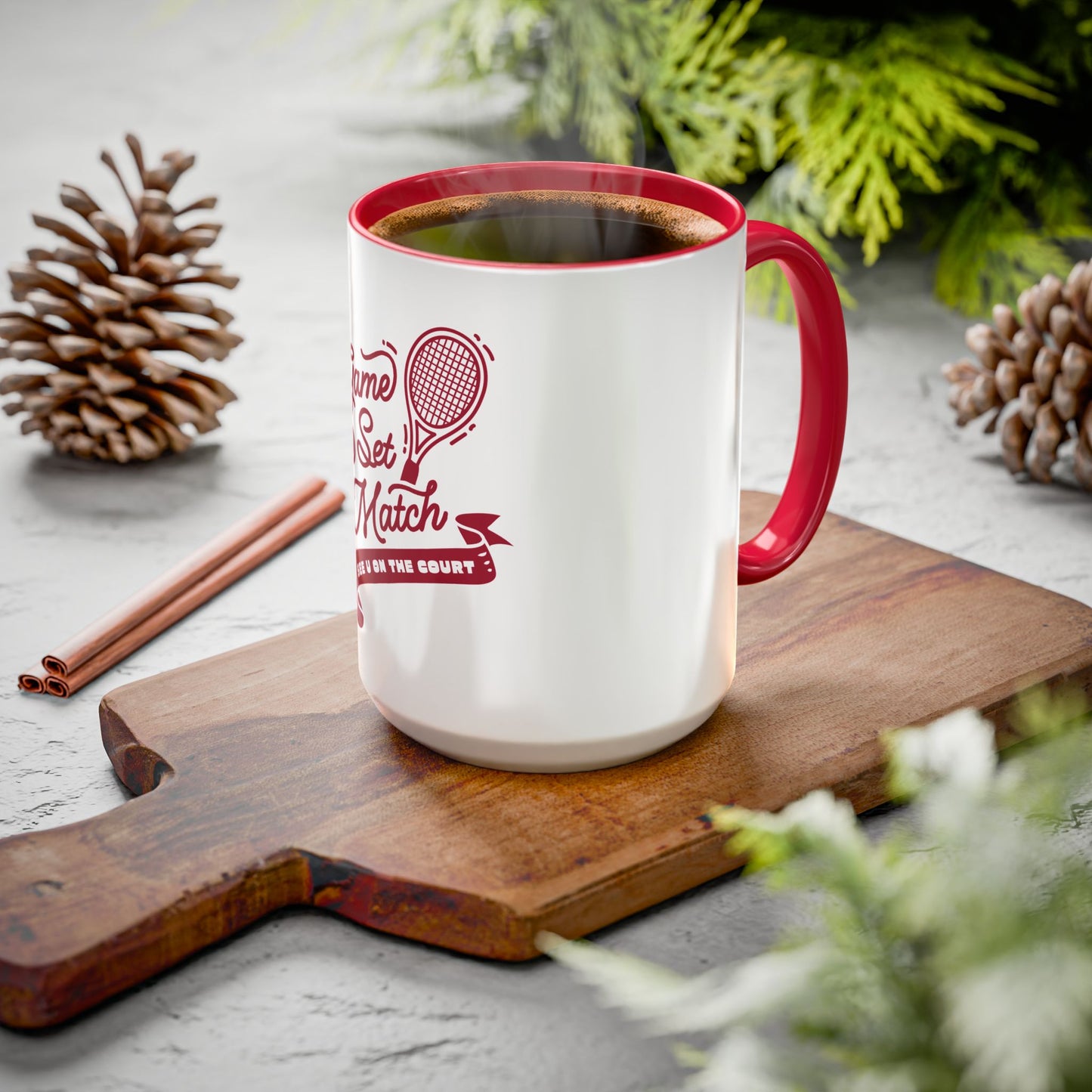White mug with red handle and interior, featuring a tennis-themed design, on a wooden cutting board with Christmas decor.