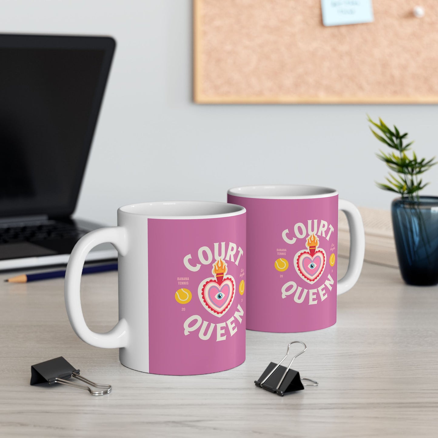 Two pink mugs with 'Court Queen' design on a desk with office supplies.