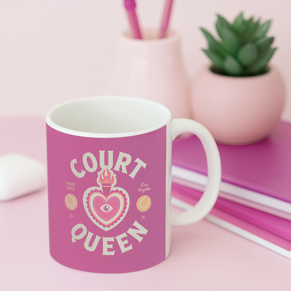 Pink mug with 'Court Queen' design on a pink surface with a plant and books in the background