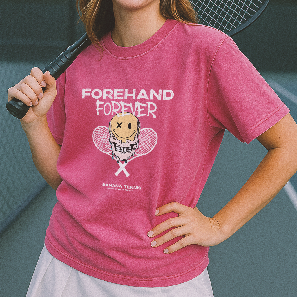 Person wearing a pink t-shirt with a graphic design and text, holding a tennis racket.
