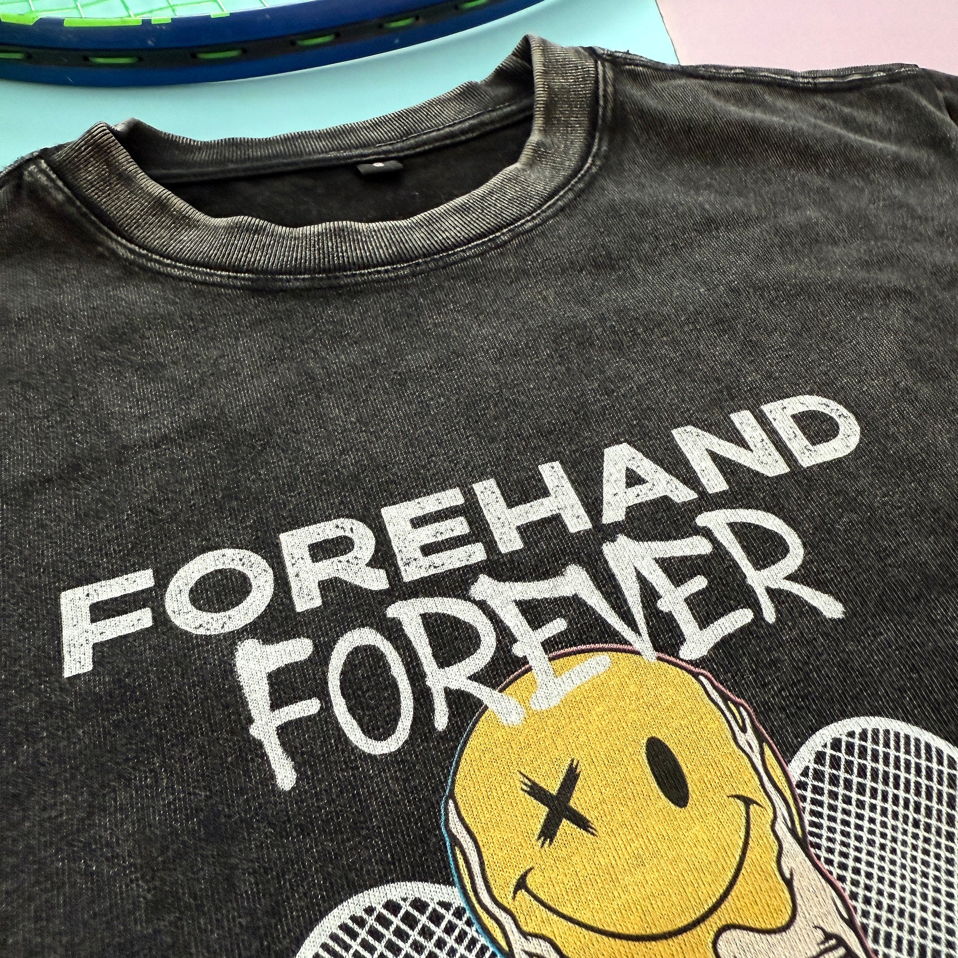 Black t-shirt with 'Forehand Forever' text and smiley face design on a light pink background
