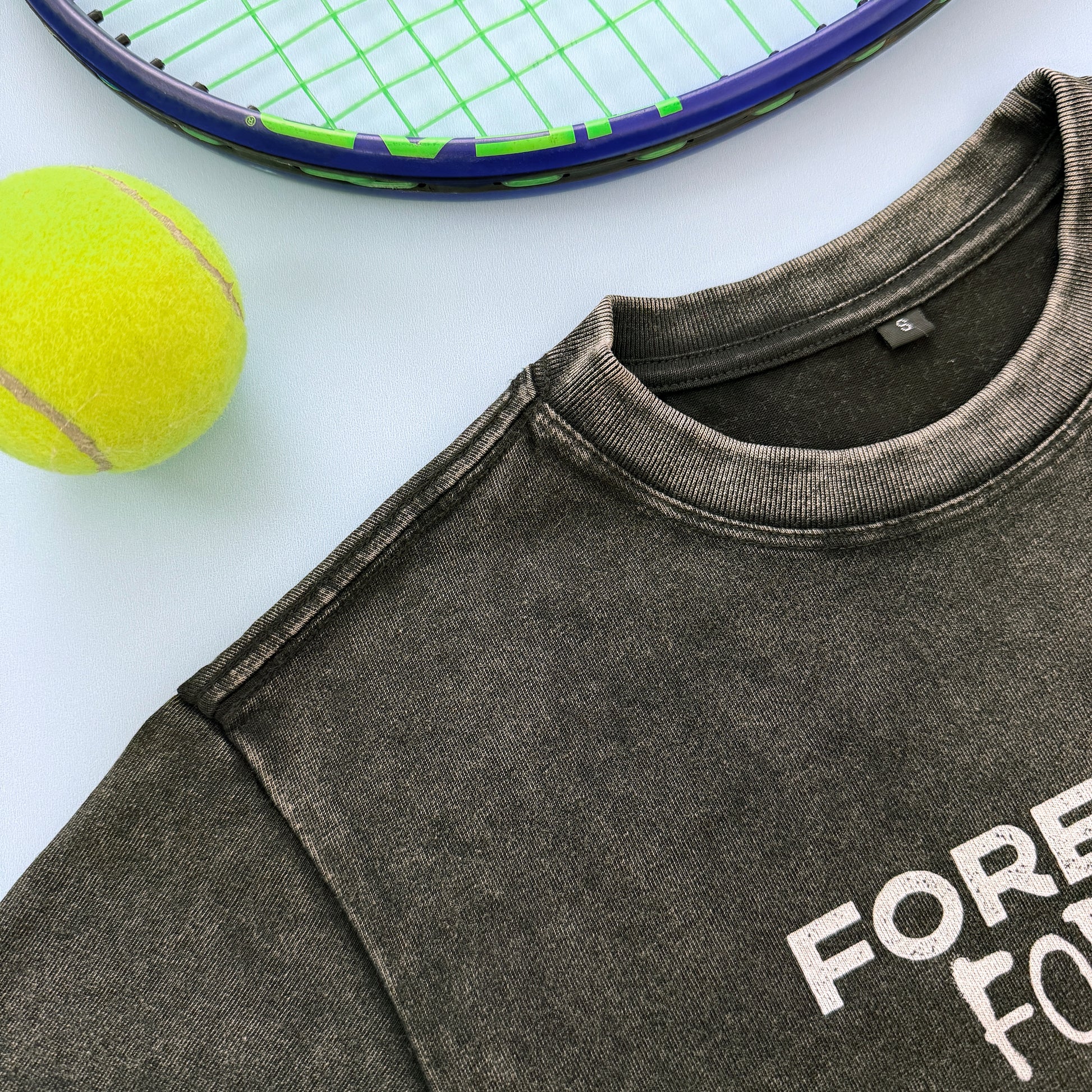 Gray sweatshirt with FOREHAND FOREVER text, tennis ball, and racket on a light background