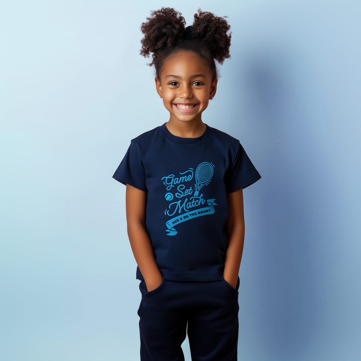 Girl in navy youth t-shirt with blue 'Game Set Match' design and tennis graphic, standing against light blue background