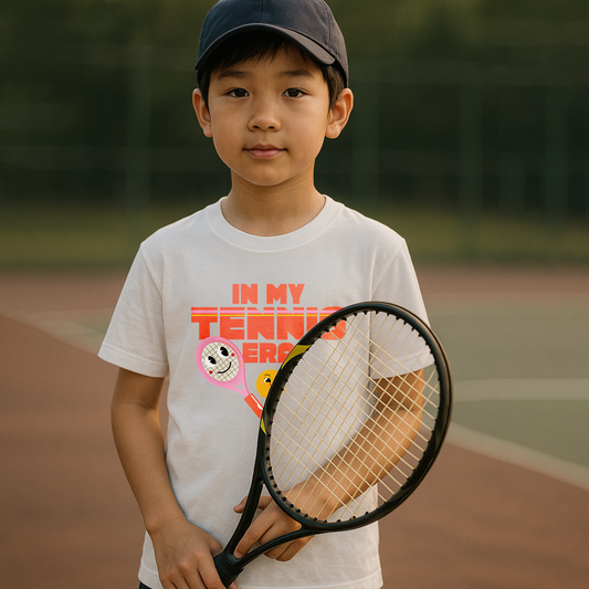 Young boy wearing white 'IN MY TENNIS ERA' tee with tennis ball emoji, standing on tennis court holding racquet
