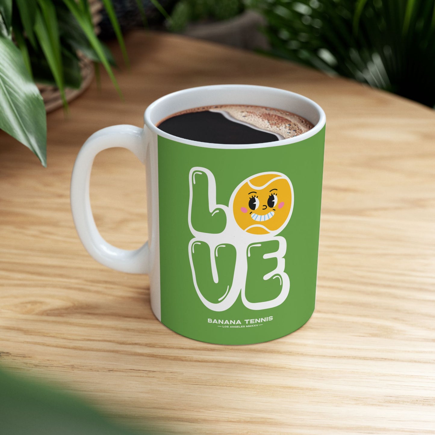 Green mug with 'LOVE' and cartoon face design on a wooden table