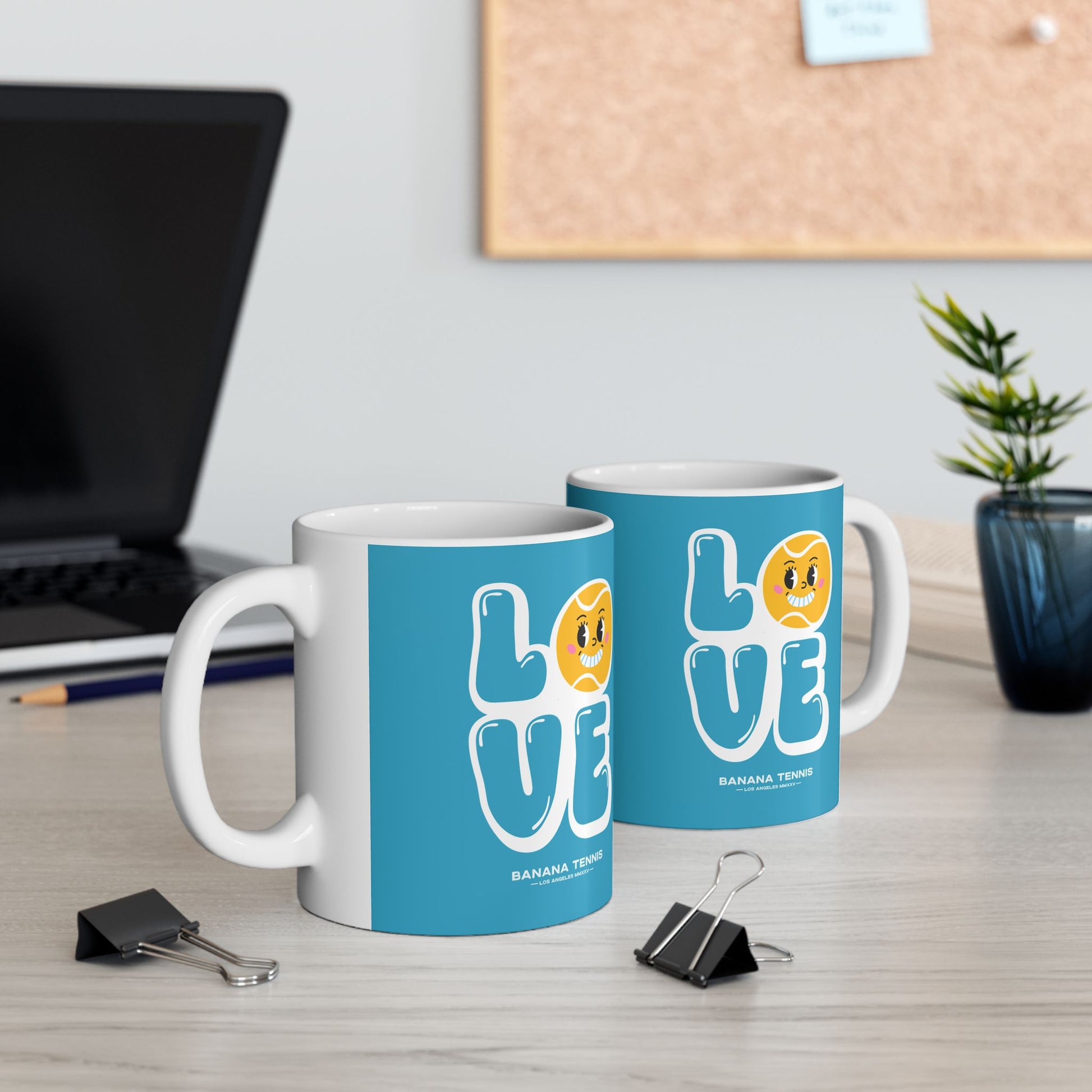 Two mugs with 'LOVE' design on a desk with office supplies and a plant.
