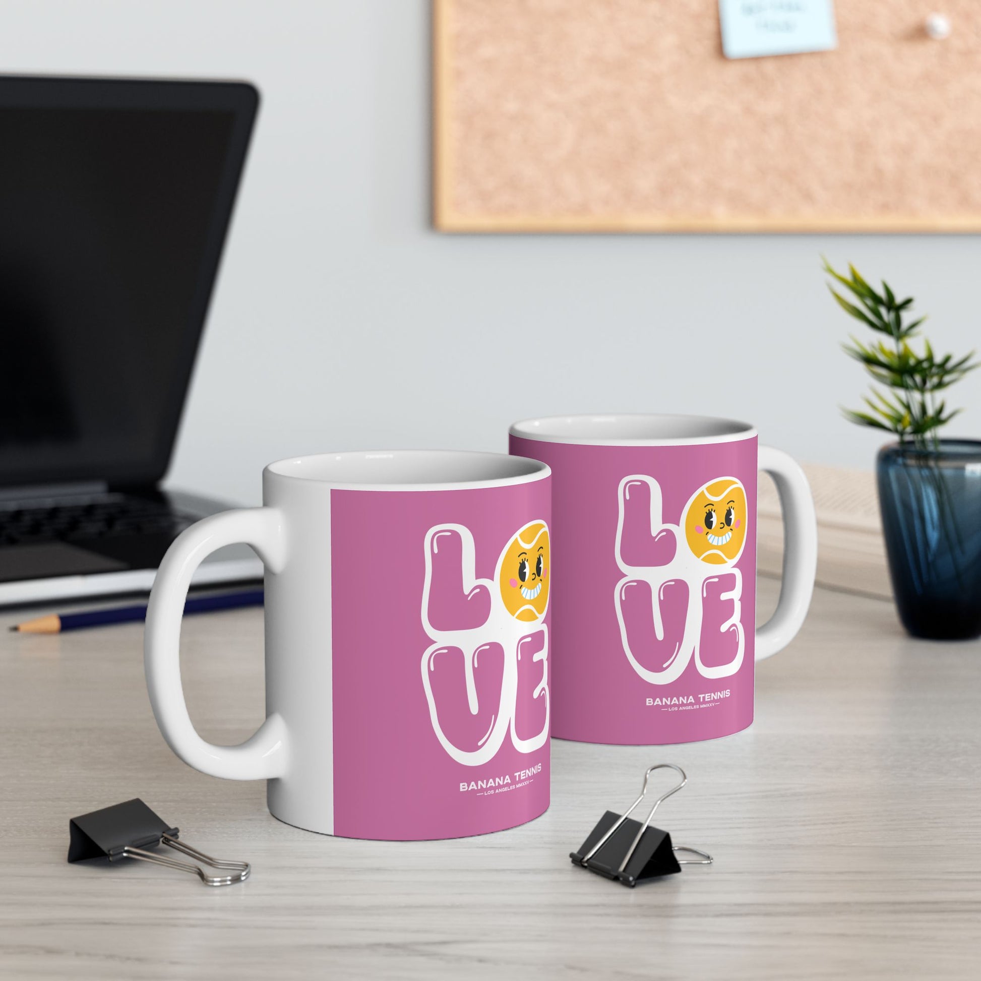 Two mugs with 'LOVE' design on a desk with office supplies and a plant.