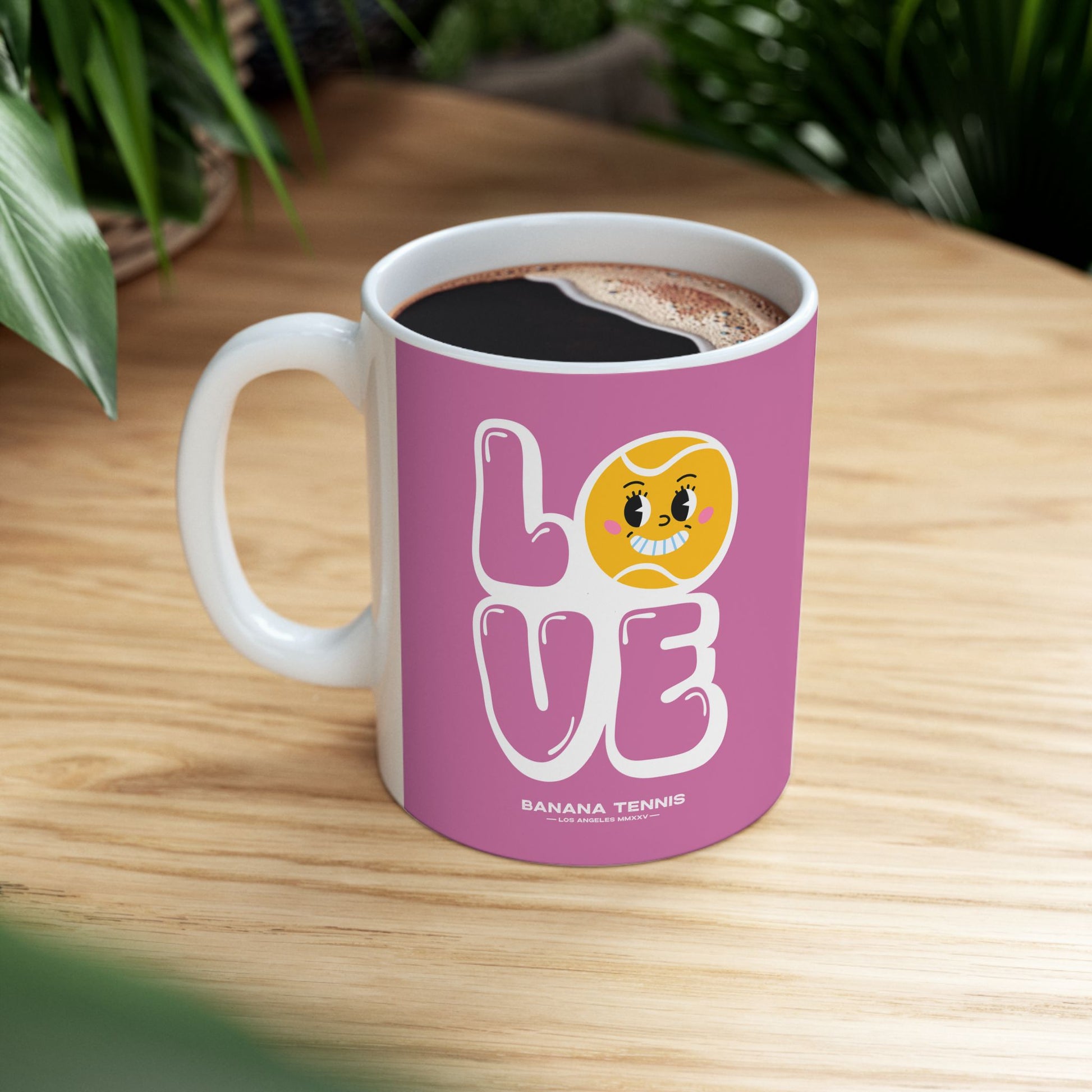 Pink mug with 'LOVE' and banana tennis character on a wooden table