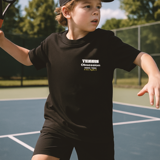 Child playing tennis on a court wearing a black t-shirt with 'Tennis Obsession' text.