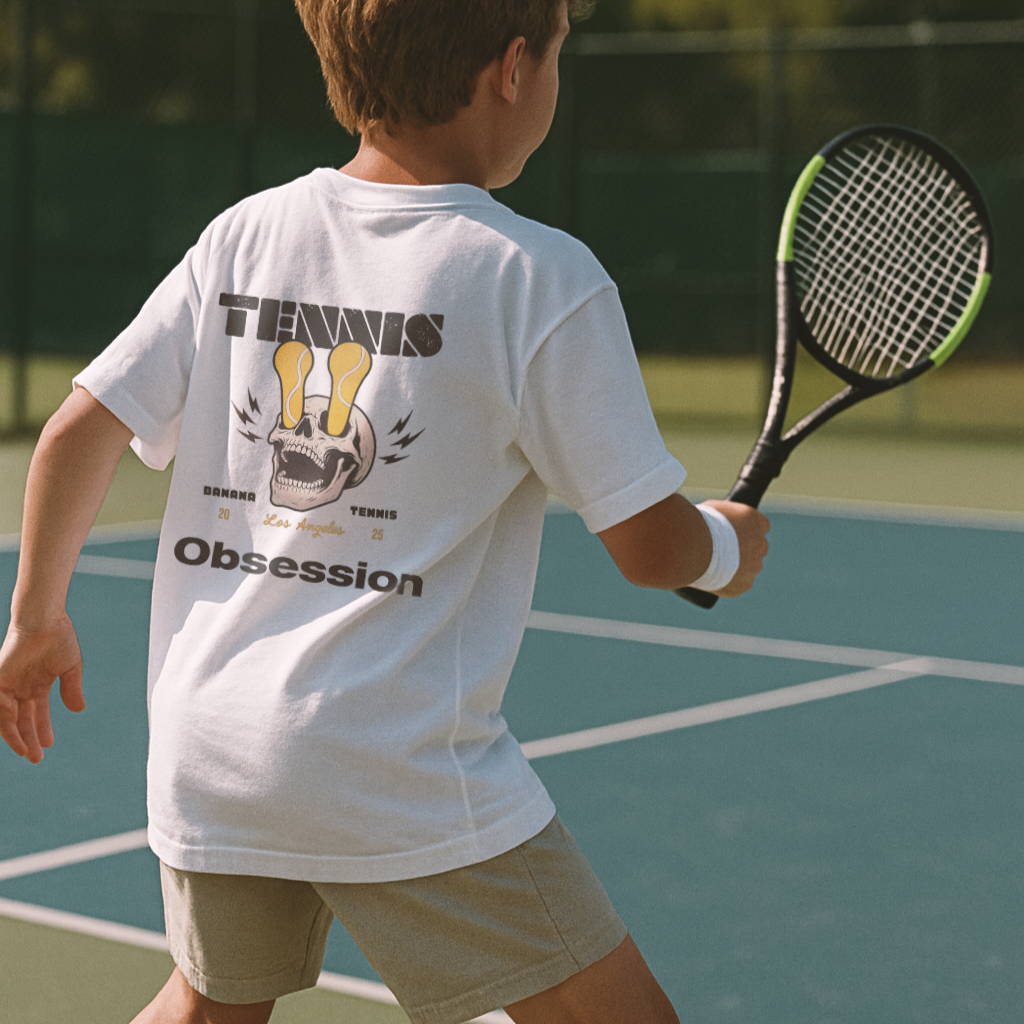 Child on a tennis court wearing a white t-shirt with 'Tennis Obsession' text.