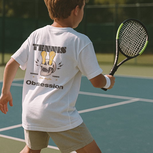 Child on a tennis court wearing a white t-shirt with 'Tennis Obsession' text.