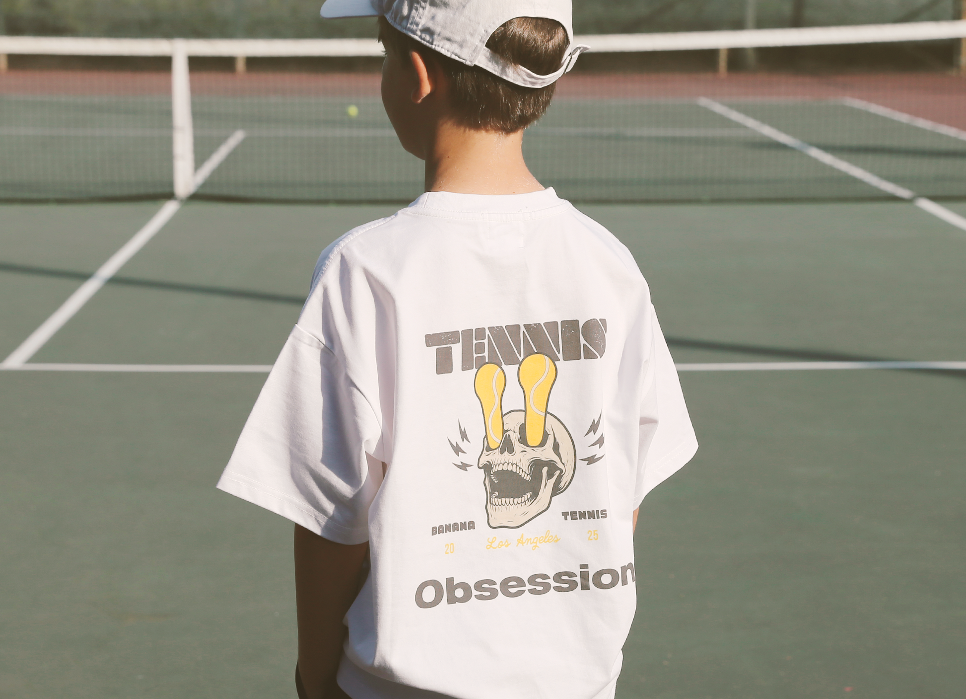 Person wearing a white t-shirt with 'Tennis Obsession' design on a tennis court