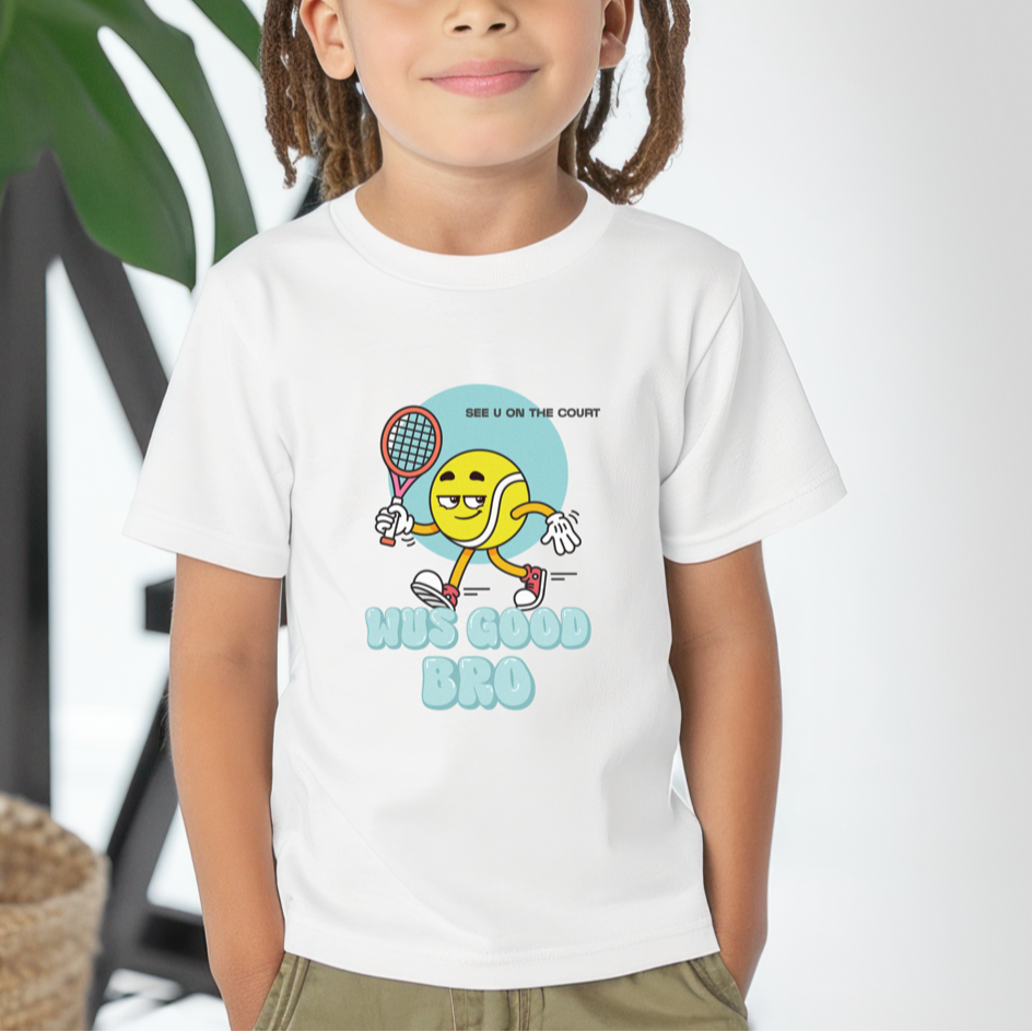 Child wearing white 'WUS GOOD BRO' t-shirt featuring playful yellow tennis ball cartoon holding a racket, shown against white background and plant
